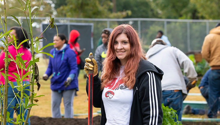 Miranda stands with a shovel in the community garden