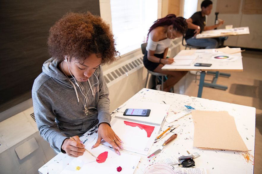 2 students work on art projects at a desk.