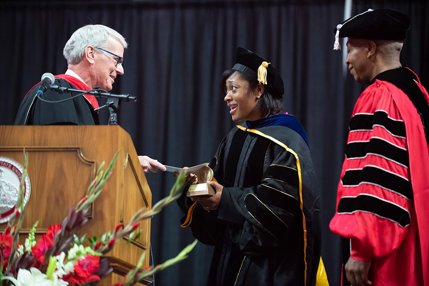 David Powers from the podium presents award to Dr. Dance-Barnes 